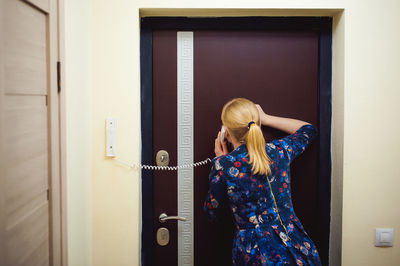 Rear view of woman talking on telephone while standing against door