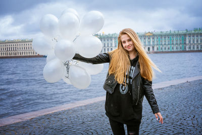 Caucasian girl holding white balloons standing by the river on the embankment