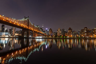 Illuminated buildings by river against sky at night