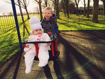 Cute brother boy pushing sister in swing at playground