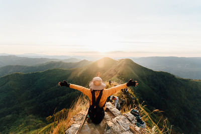 Rear view of woman with arms outstretched on mountain against sky