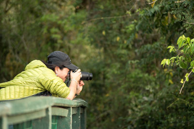 Side view of woman photographing with digital camera in forest