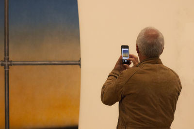 Rear view of man photographing against wall