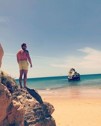 Shirtless man standing at beach against sky