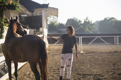 Woman touching horse with animal care equipment while standing at ranch