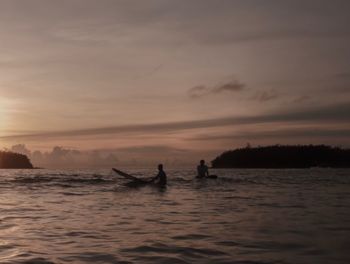 Silhouette man in sea against sky during sunset