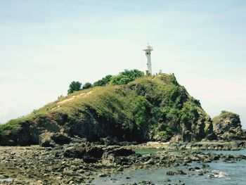 Lighthouse amidst rocks and sea against sky