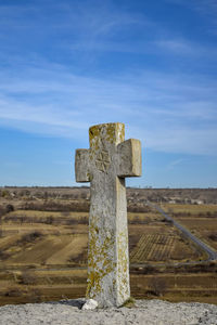 Ancient stone christian cross, mounted on cliff, near rock monastery, against blue sky.
