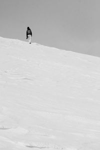 Distant view of person walking on snowy mountain against sky
