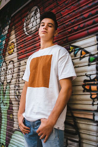 Portrait of young man standing against graffiti wall