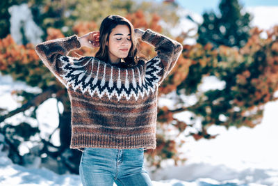 Smiling woman with eyes closed standing against trees during winter