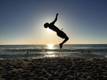 Silhouette man jumping on beach against sky during sunset