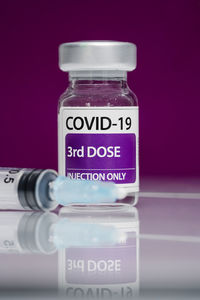 Medical syringe and glass vial of 3d doses booster of coronavirus vaccine placed against purple background