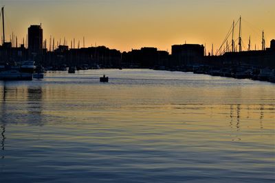 Silhouette buildings by sea against sky during sunset