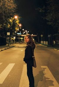 Rear view of woman standing on road at night