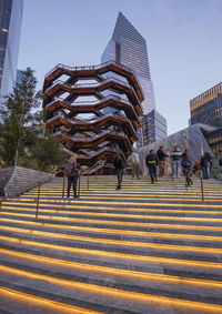 People on staircase against buildings in city against sky