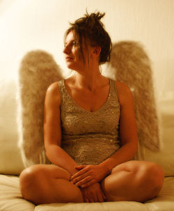 Young woman in angel costume looking away while sitting on bed