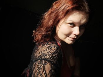 Close-up portrait of smiling young woman against black background