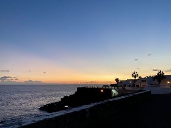 Silhouette city by sea against romantic sky at sunset