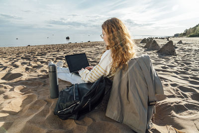 Young woman using laptop at beach on sunny day