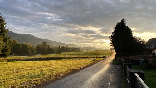 Empty road amidst field against sky during sunset