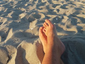 Low section of person relaxing on sand at beach