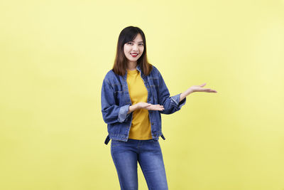 Portrait of young woman standing against yellow background