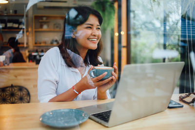 Smiling businesswoman using technology while holding coffee at cafe