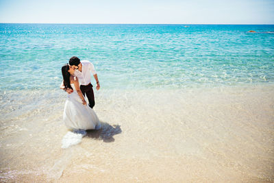 Bride kissing groom while standing on shore at beach