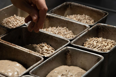 Close-up of female hands sprinkling a piece of raw dough in a baking form with seeds and sunflower