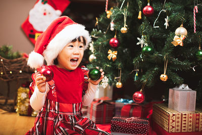 Smiling girl holding decoration by christmas tree