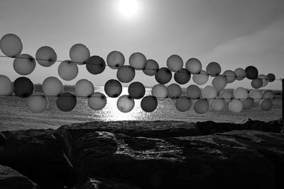 Balloons on rocks by sea against sky