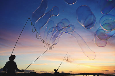 Low angle view of man with bubbles against sky during sunset