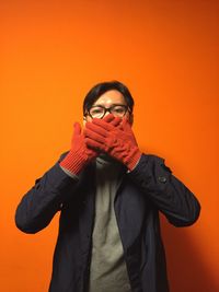 Portrait of young man standing against orange background