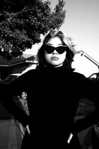 Portrait of young woman wearing sunglasses standing against sky