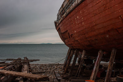 Abandoned boat by sea against sky