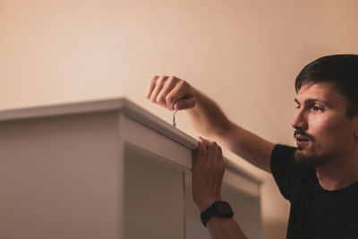 A young man is screwing a screw into a board with a curly screwdriver.