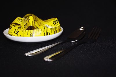 Close-up of yellow tape measure in plate by cutlery on table