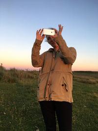 Woman photographing with mobile phone on field during sunset