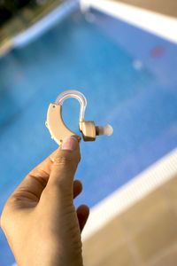 Close-up of human hand holding hearing aid over swimming pool