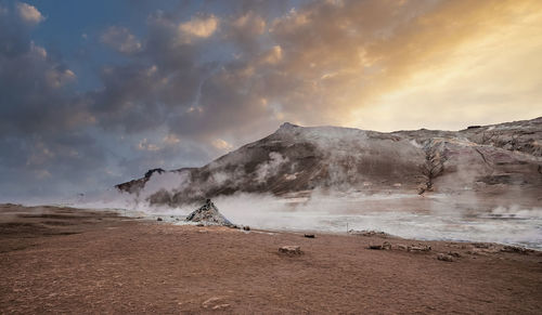 Steam emitting from crater in geothermal area of hverir against sky during sunset