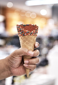 Close-up of hand holding ice cream cone with sprinkles