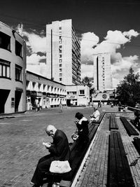 People sitting on footpath amidst buildings in city