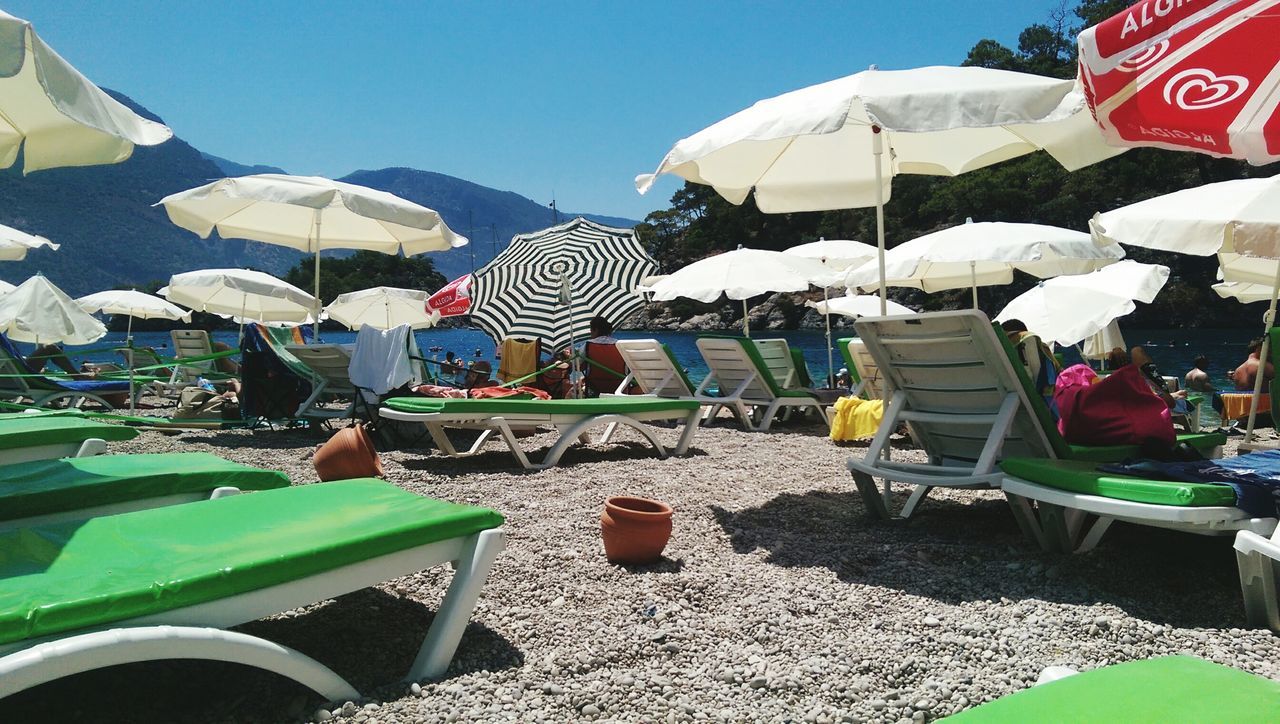 beach umbrella, sunshade, sunlight, parasol, beach, clear sky, day, vacations, umbrella, outdoors, tent, incidental people, in a row, blue, person, travel, men, tourism, multi colored