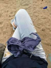 Low section of woman knitting while sitting on beach 