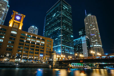 Illuminated buildings by river against sky at night