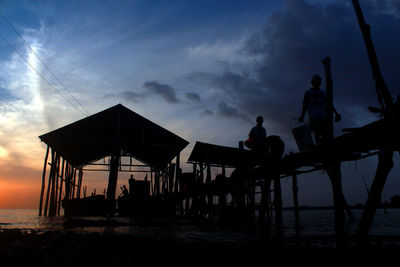 Silhouette of fishermen standing on pier at sunset