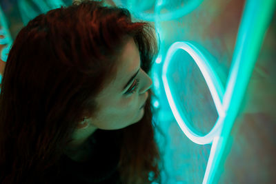 Stylish long haired brunette in casual wear looking away among neon signs at city street