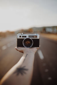 Crop hand of person with vintage camera on palm between asphalt route on blurred background