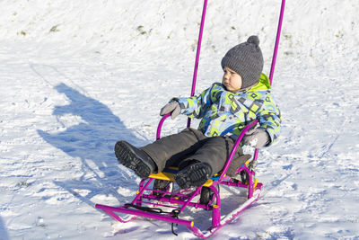 Full length of cute boy sitting on sled